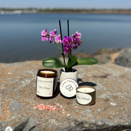 amber glass candle jar. golden tin candle container. orchid vase in background. on rocky waterfront