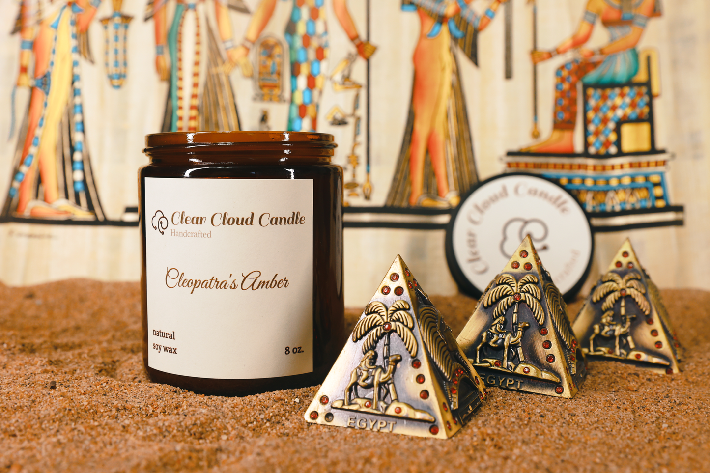 scented candle in amber glass jar, scent name: cleopatra's amber. ancient Egyptian props, mini pyramids, sand ground