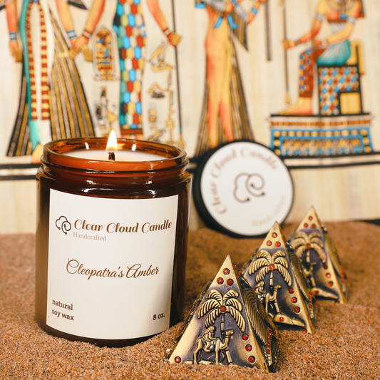 lit scented candle in amber glass jar, scent name: cleopatra's amber. ancient Egyptian props, mini pyramids, sand ground