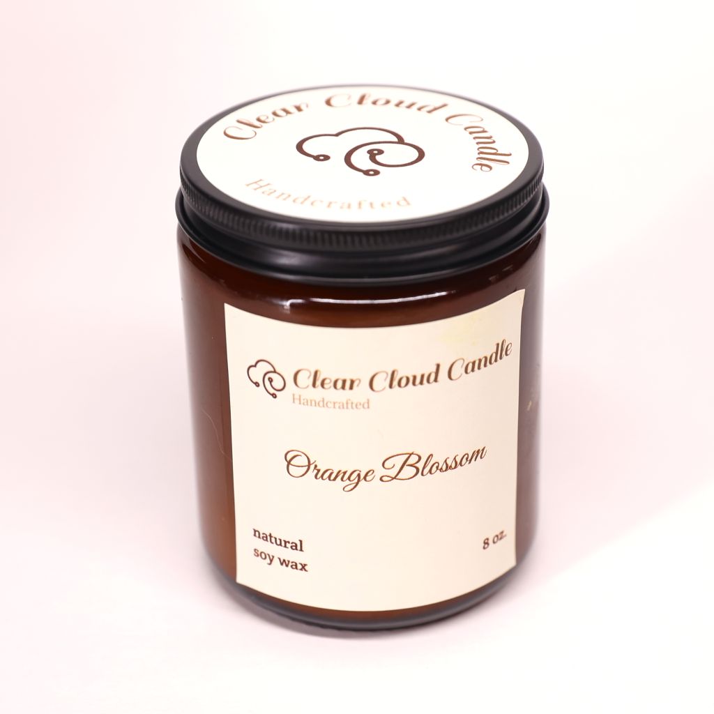Amber jar with cream label of 'Orange Blossom' candle from Clear Cloud Candle on a white background