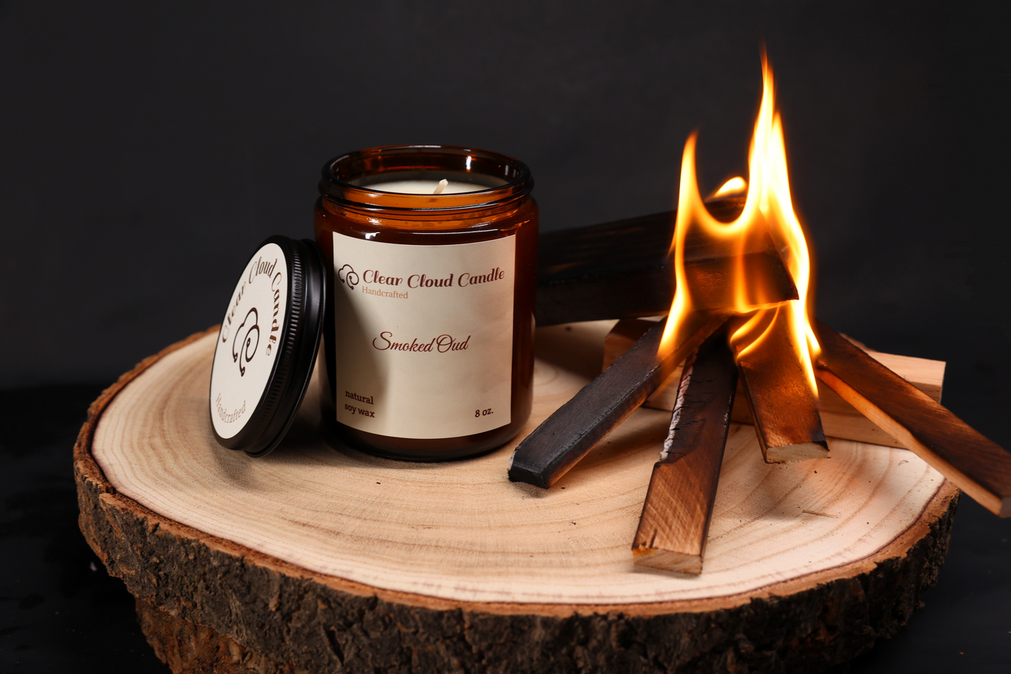 candle in amber glass jar. white wax. light cream label. wood on fire. smoke. flames. cent name: smoked oud