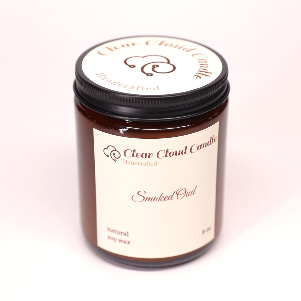 amber color candle jar with cream label from "Clear Cloud Candle" Co. with 'Smoked Oud' fragrance on a white background