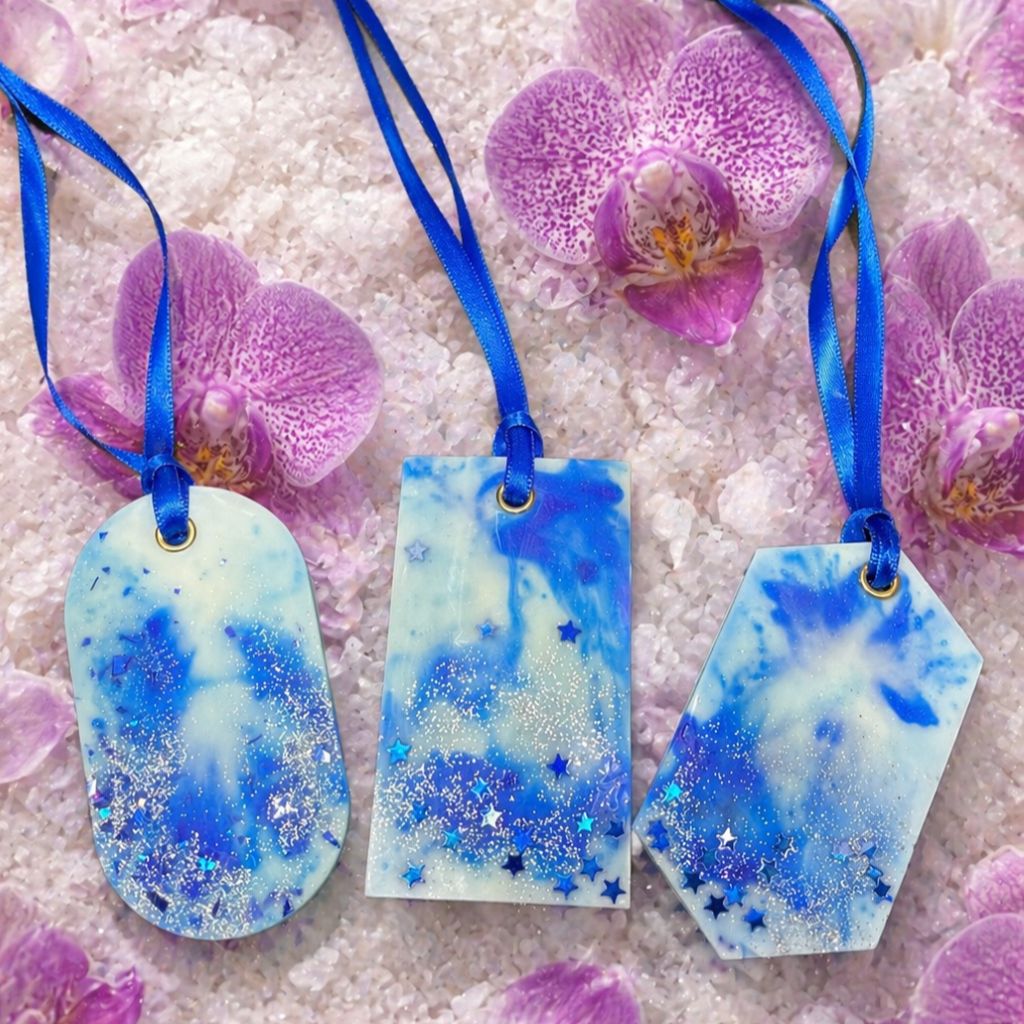 Three blue and white marbled wax closet fresheners with ribbons on a white surface with pink Orchids.