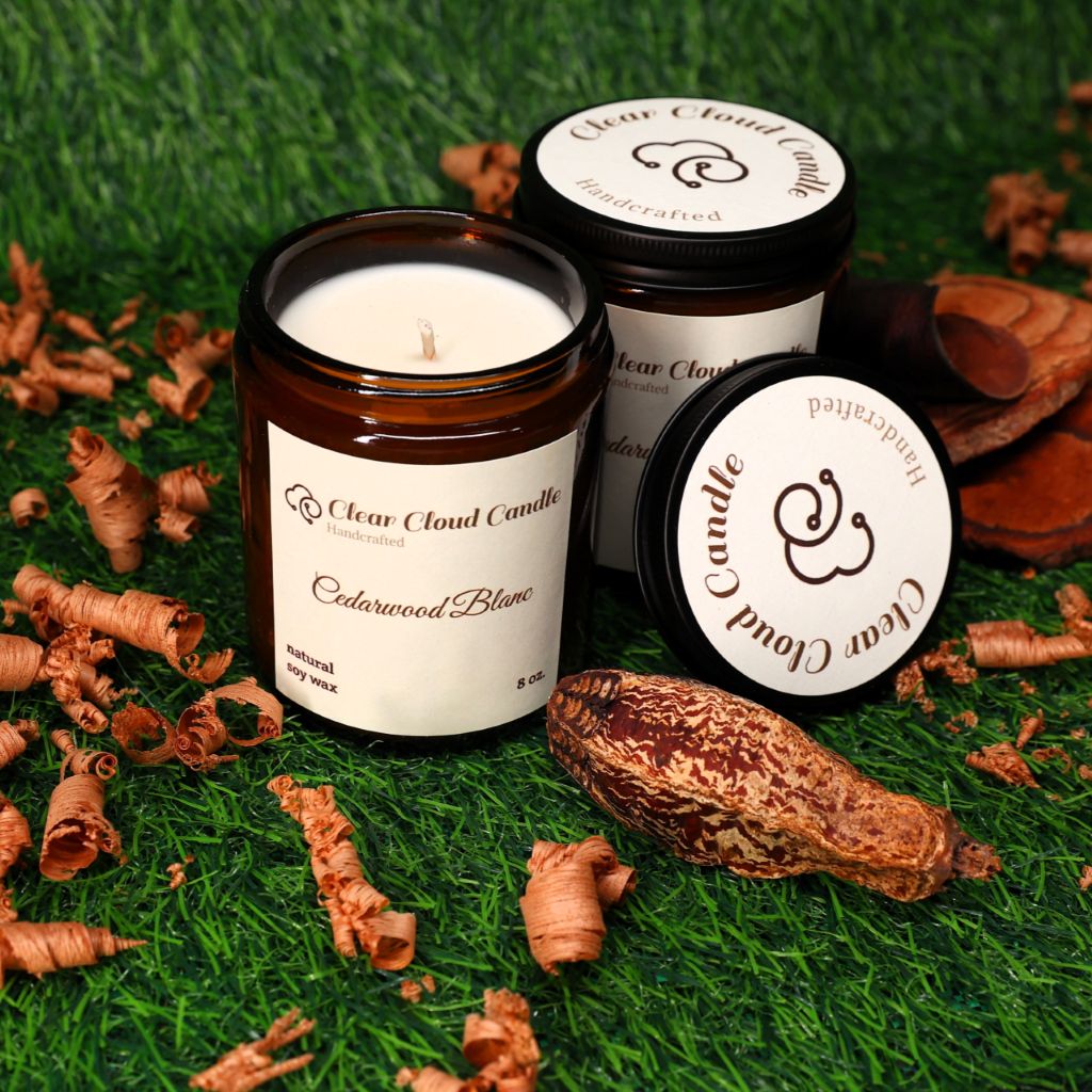 Cedarwood scented candle with 'Clear Cloud Candle' branding on a grassy background with cedarwood pieces, shavings, and nut.