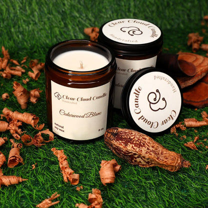 Cedarwood scented candle with 'Clear Cloud Candle' branding on a grassy background with cedarwood pieces, shavings, and nut.