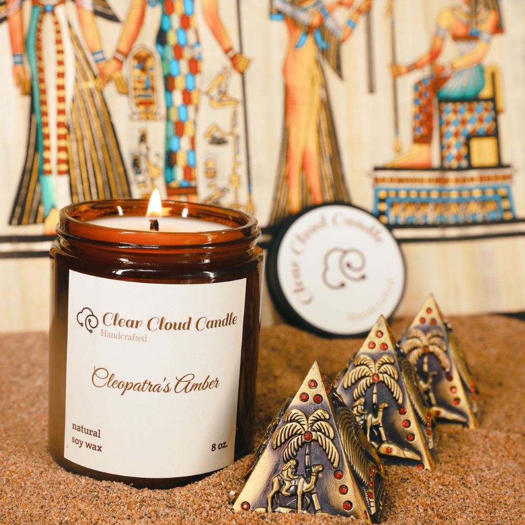 scented candle in amber glass jar, scent name: cleopatra's amber. ancient Egyptian props, mini pyramids, sand ground