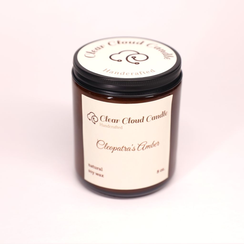 Amber color candle jar with "Clear Cloud Candle" Co. label with scent named "Cleopatra's Amber" on a white background