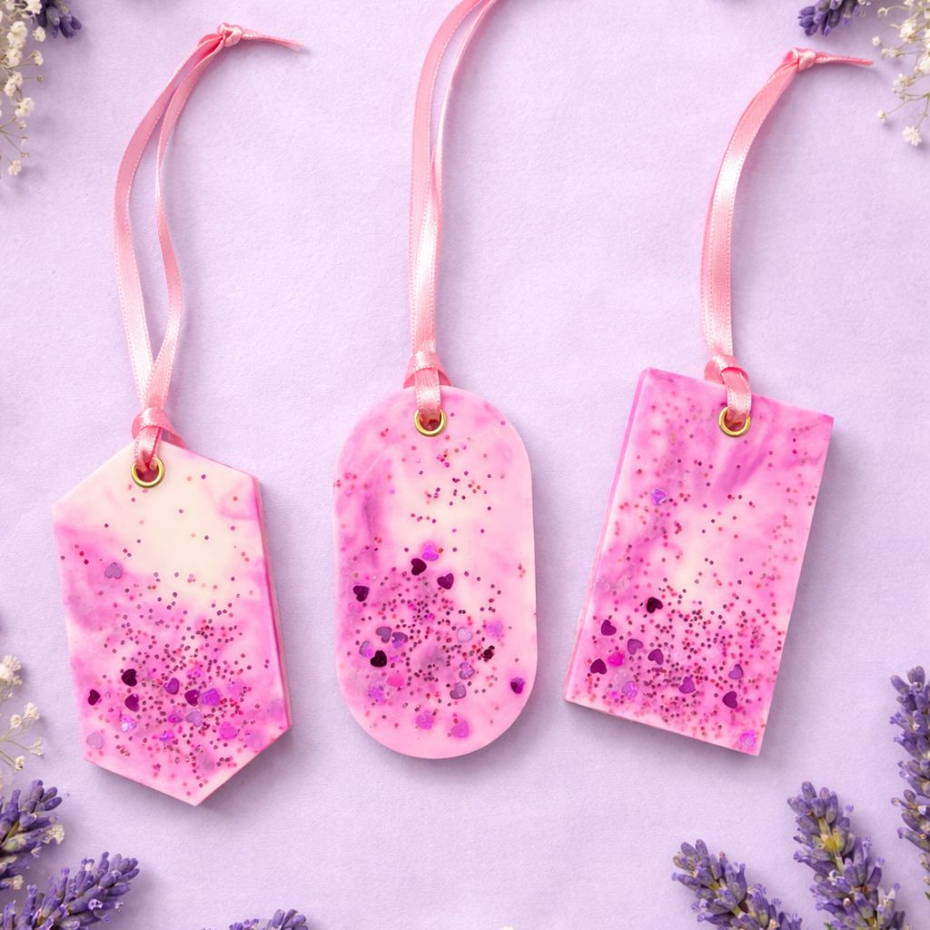 Three pink speckled wax closet fresheners with ribbons on a light purple background with lavender flowers.