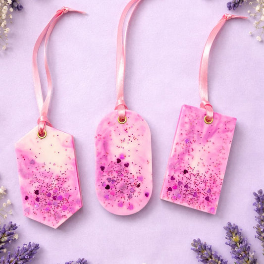 Three pink speckled wax closet fresheners with ribbons on a light purple background with lavender flowers.