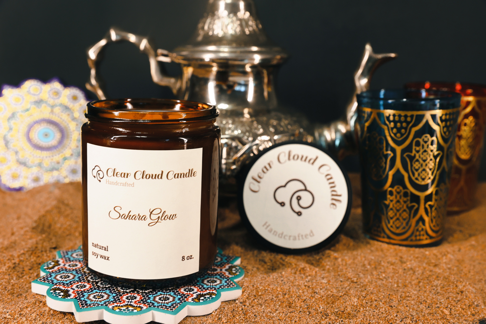 scented candle amber glass jar. Moroccan props. sand ground. candle name: sahara glow