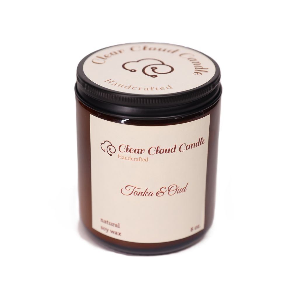 amber color candle jar with cream color label from "Clear Cloud Candle" Co. Scent name is "Tonka & Oud" on a white background.
