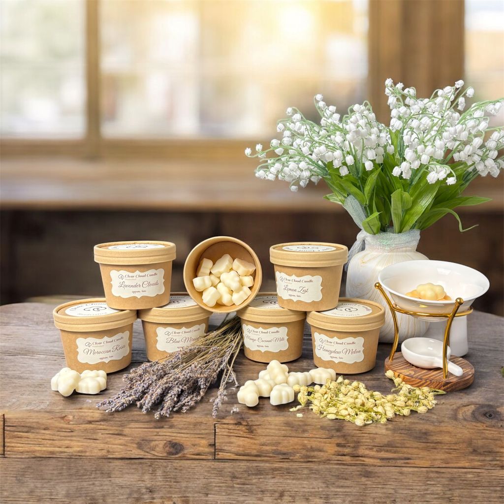 set of kraft-paper colored containers from "Clear Cloud Candle" with lids and labels reading various scents names on a wooden surface, surrounded by flowers and wax Melter. one of the containers is uncovered with cloud-shaped wax melts visible inside.